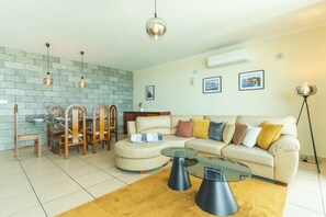 Ein Wohnzimmer mit Sofa, Couchtisch, Esstisch, Stühlen und Pendelleuchten.