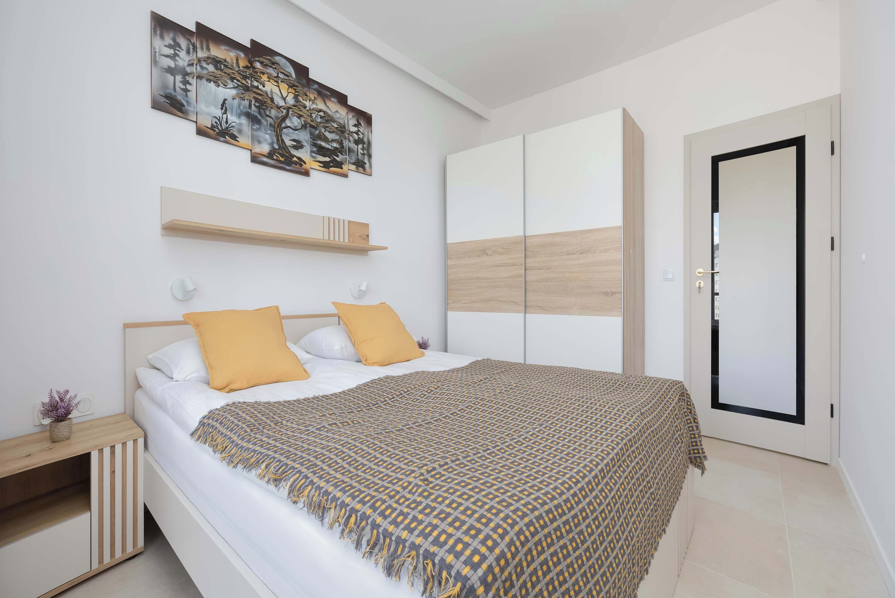 A modern bedroom with a bed, a wardrobe, a bedside table, and a wall-mounted shelf.
