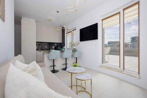 A modern living room with a sofa, two round tables, and a kitchen area in the background. - Family Apartment with Terrace | 2 Bedrooms | Balcony (Warszawa)