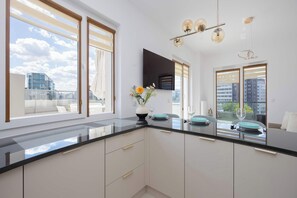 A modern kitchen with a black countertop, white cabinets, and a large window with blinds. - Family Apartment with Terrace | 2 Bedrooms | Balcony (Warszawa)