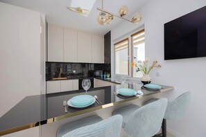 A modern kitchen with a black countertop, white cabinets, and a dining area with light blue chairs and a glass table. - Family Apartment with Terrace | 2 Bedrooms | Balcony (Warszawa)