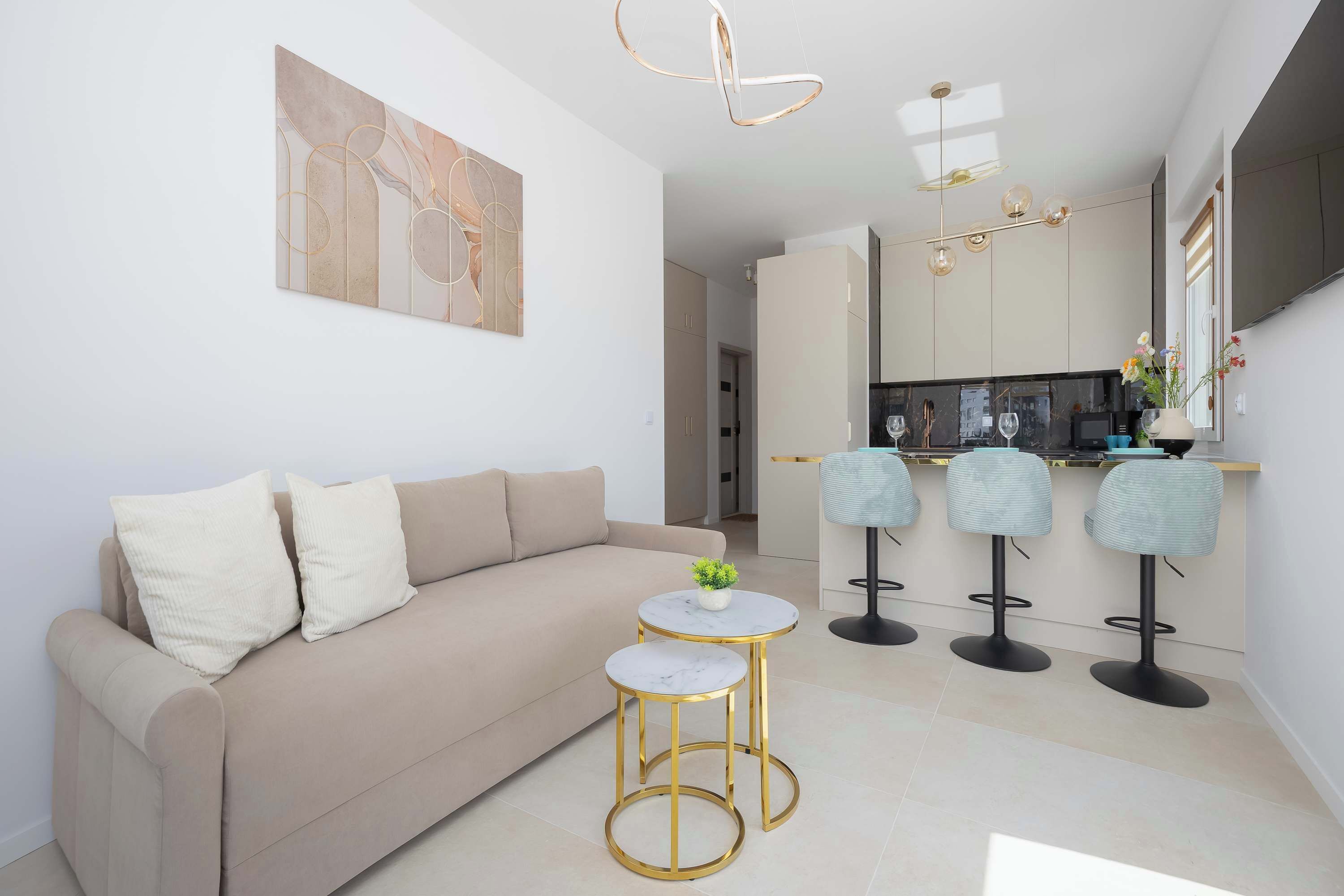 A modern living room with a sofa, two round tables, and a kitchen area with bar stools.