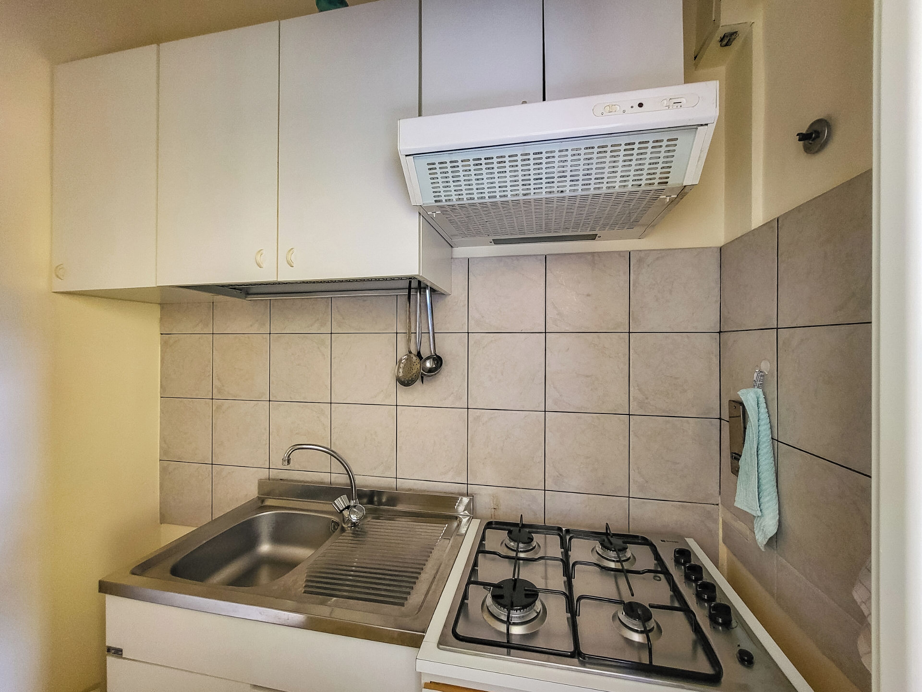 A kitchen with a stainless steel sink, a gas stove, and white cabinets.