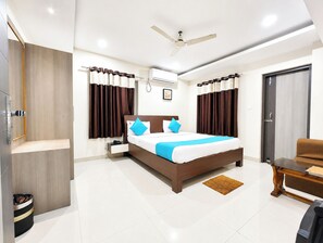 A modern hotel room with a large bed, a ceiling fan, an air conditioning unit, a wooden wardrobe, a small table, and a door. - Hotel Shivangi Inn Puri (Puri)
