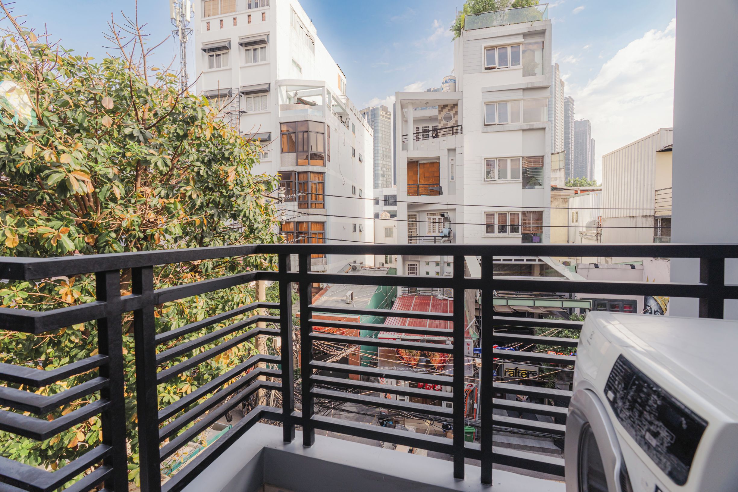 A balcony with a view of multi-story buildings, a tree, and a white air conditioning unit.