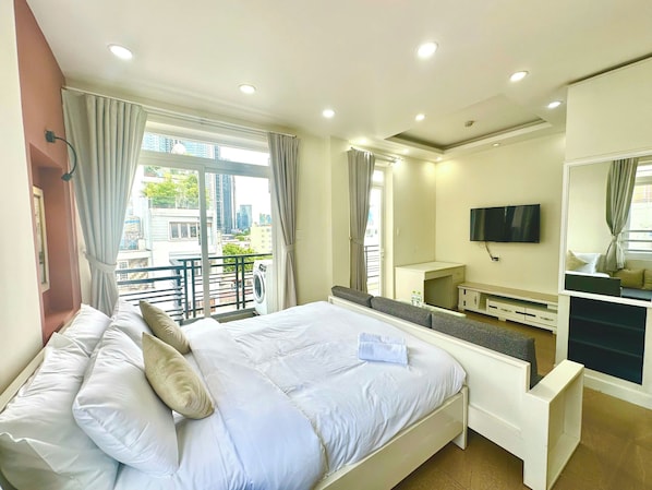 Ein Hotelzimmer mit Bett, Schreibtisch, Fernseher und einem Balkon mit Blick auf die Stadt.