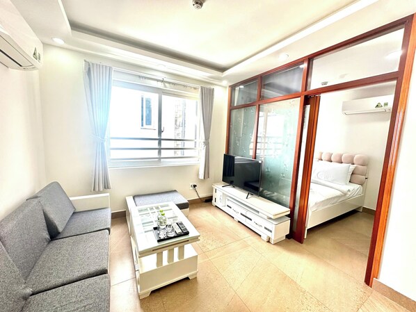 Una sala de estar moderna con sofá, mesa de centro, televisor y una cama con cabecera.