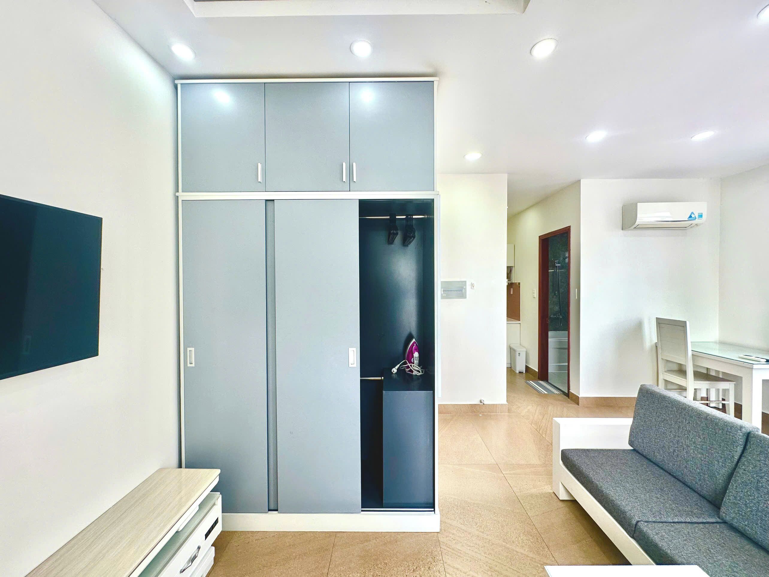A modern living room with a grey sofa, a flat-screen TV mounted on the wall, and a built-in wardrobe with a mirror.