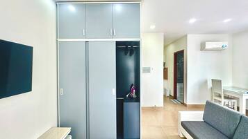 A modern living room with a grey sofa, a flat-screen TV mounted on the wall, and a built-in wardrobe with a mirror.
