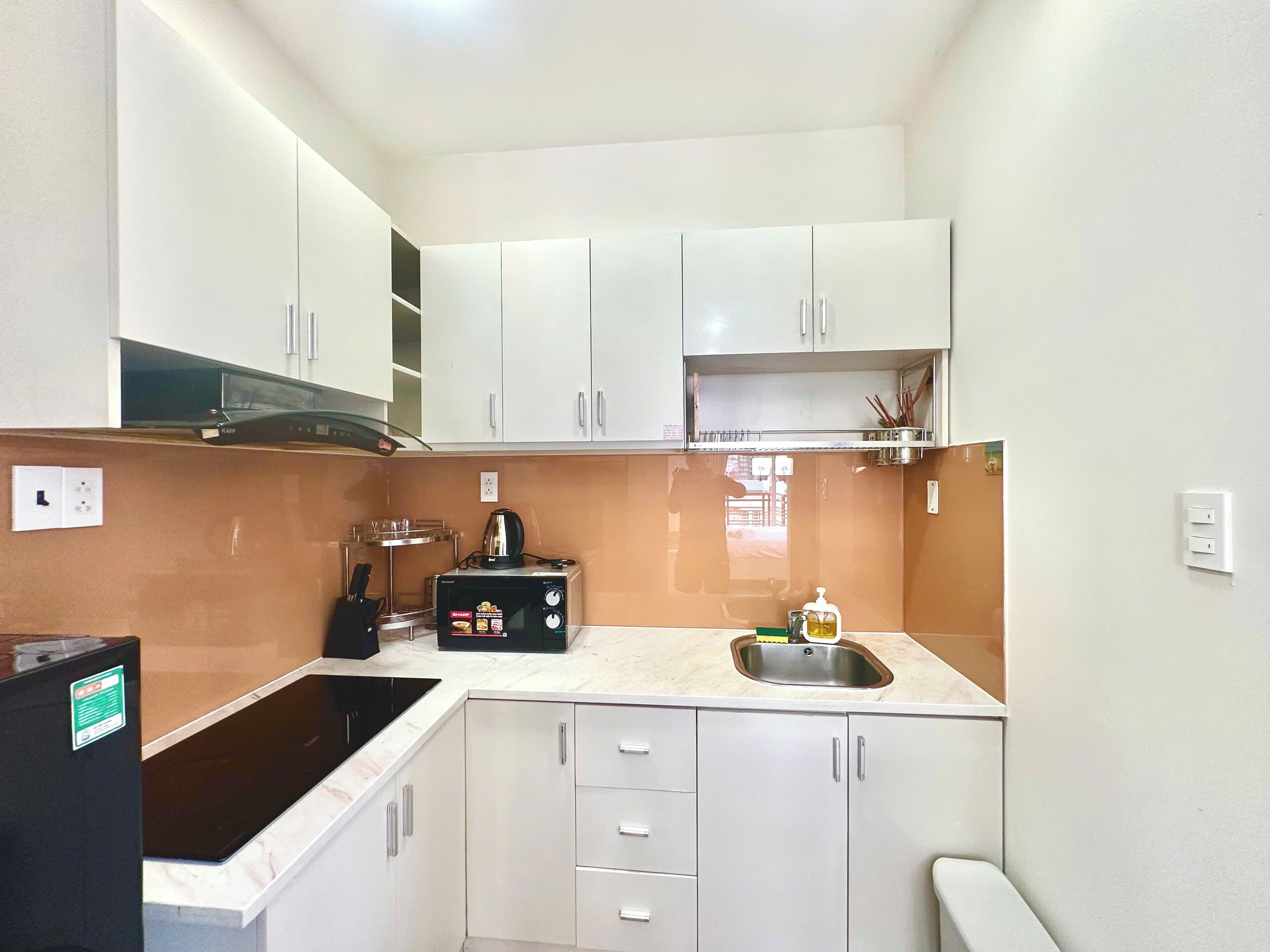 A compact kitchen with white cabinets, a black microwave, a sink, and a stove.