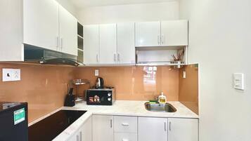 A compact kitchen with white cabinets, a black microwave, a sink, and a stove.
