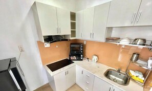 A compact kitchen with white cabinets, a black stove, a microwave, and a sink. - Serenity River Saigon (Thanh My Tay)