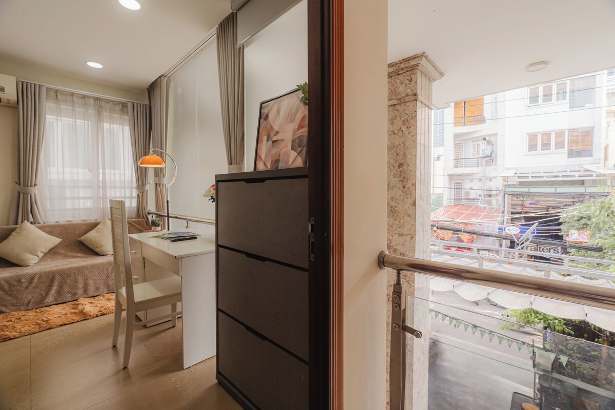Un espacio habitable compacto con kitchenette, sofá, escritorio y vista a la ciudad desde un balcón.