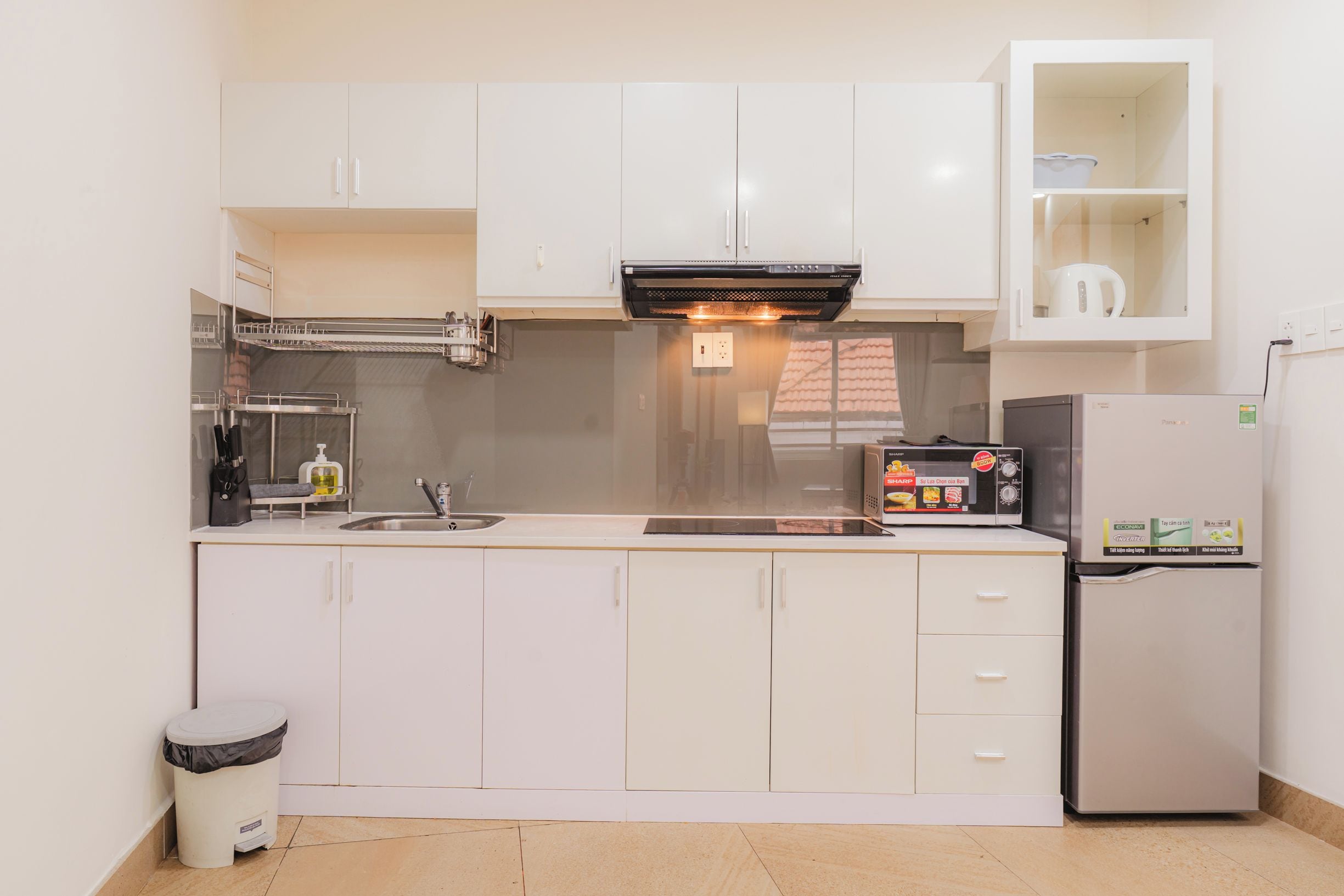 A compact kitchen with white cabinets, a stainless steel refrigerator, a built-in microwave, and a small trash bin.