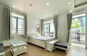 A modern bedroom with a bed, bedside tables, a bench, and large windows with curtains. - Serenity River Saigon (Thanh My Tay)