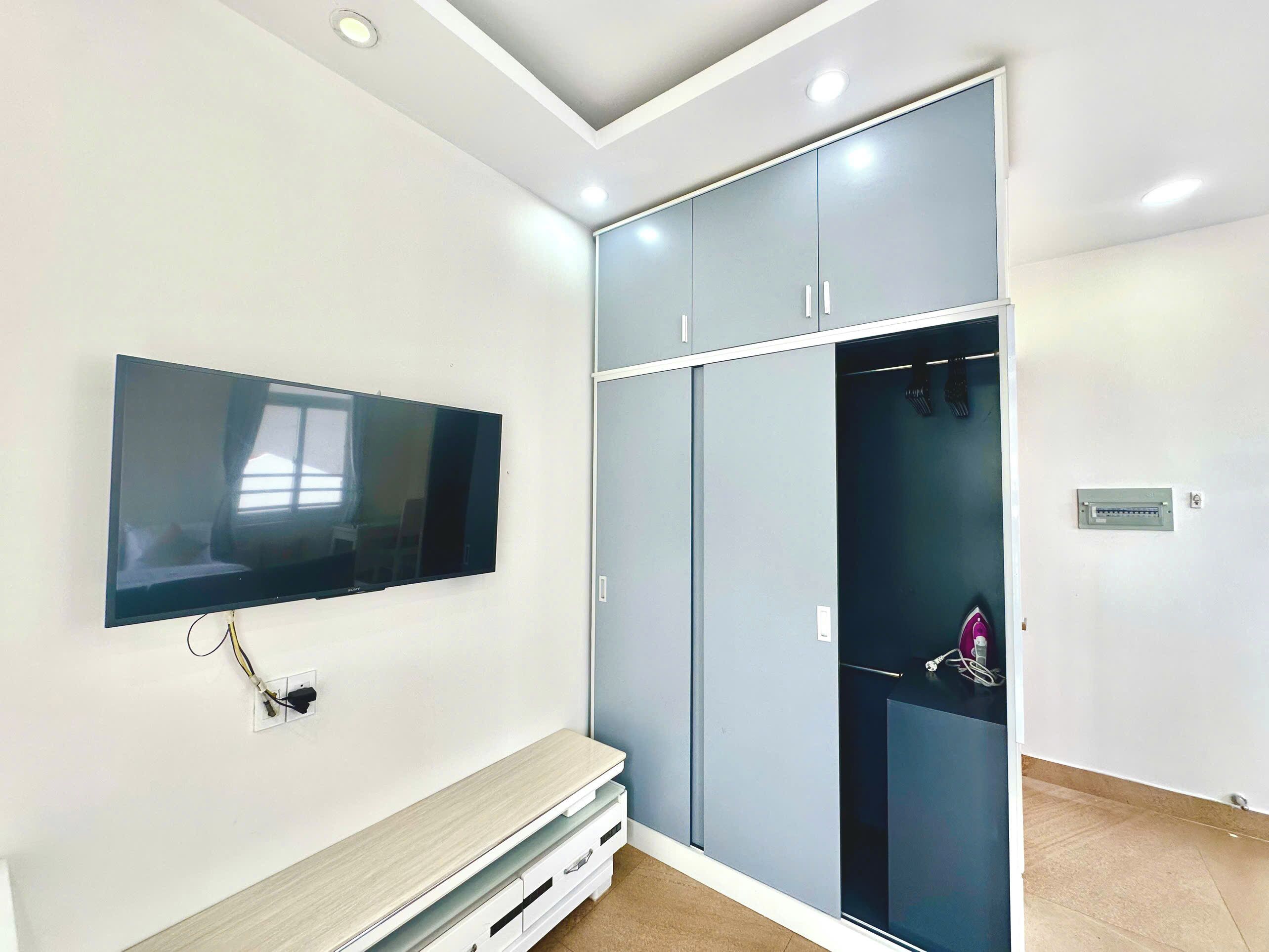 A room with a flat-screen TV mounted on the wall, a built-in bench, and a wardrobe with sliding doors.