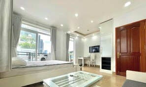 A modern hotel room with a bed, a glass coffee table, a TV, and a view of the city. - Serenity River Saigon (Thanh My Tay)
