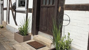 A traditional half-timbered building with a dark wooden door, a small step leading to the entrance, and two rectangular planters with plants. - Holiday Living Zennern - near Fritzlar & Edersee (Wabern)