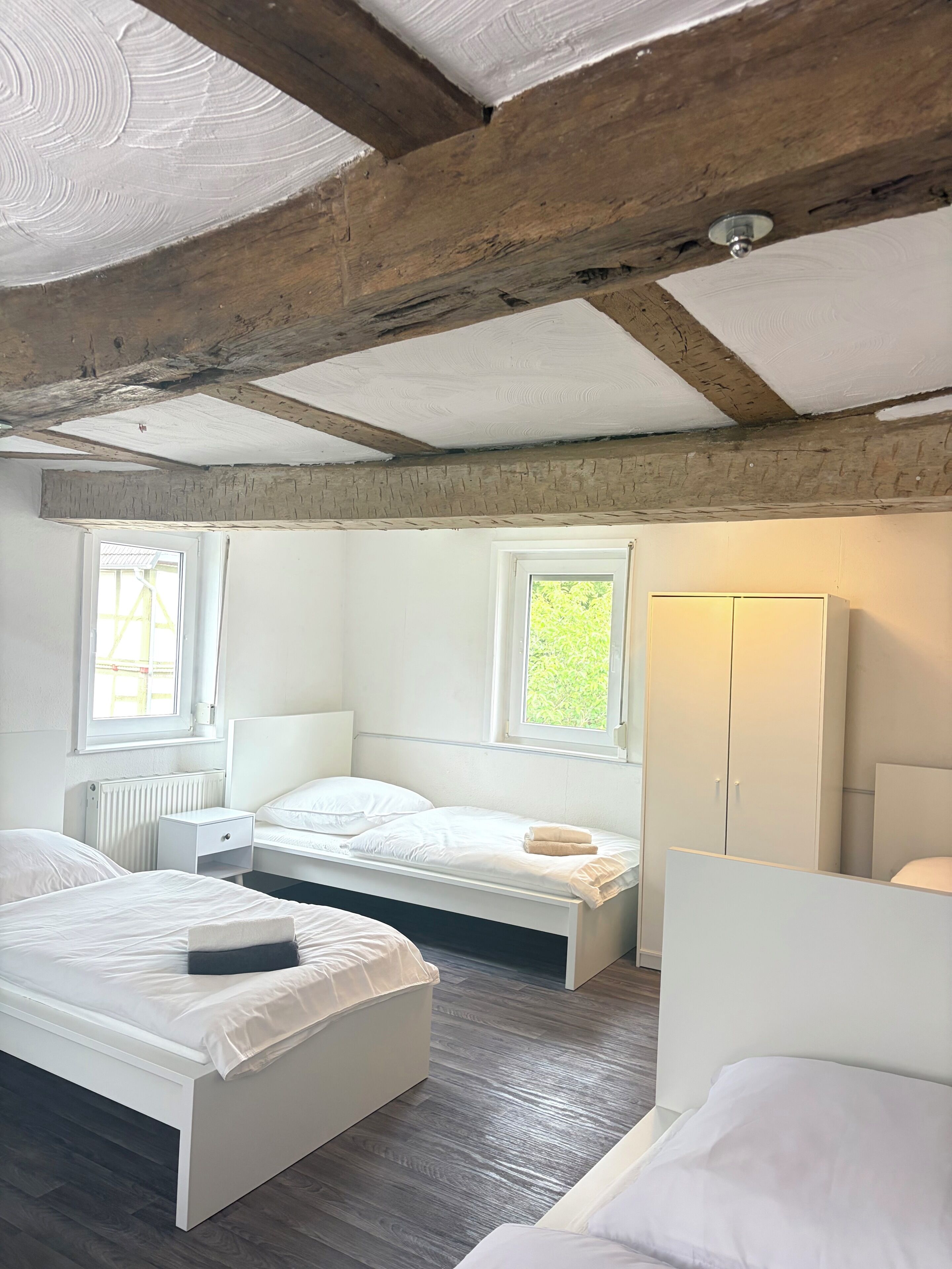 A bedroom with two beds, a window, a radiator, and a wardrobe.
