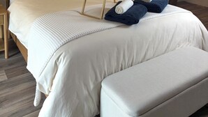 A bedroom with a wooden bed, a bedside table, a nightstand, a bench, a tray with towels, and two wall-mounted lamps. - Holiday Living Zennern - near Fritzlar & Edersee (Wabern)