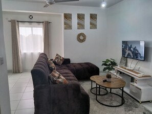 Ein Wohnzimmer mit einem Ecksofa, einem Couchtisch, einem Fernseher und einem Wanddekor.