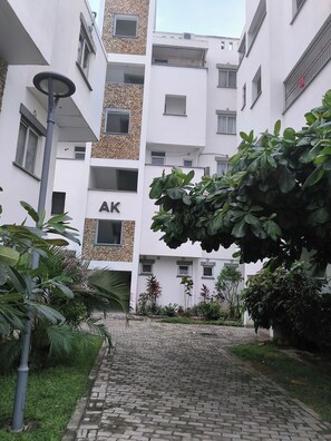 Ein mehrstöckiges Gebäude mit einem zentralen Innenhof, umgeben von Grünpflanzen und einem Kopfsteinpflasterweg.