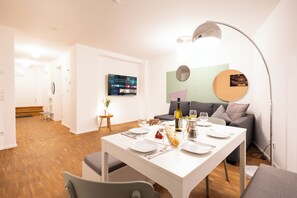 Ein moderner Essbereich mit einem weißen Tisch, gedeckt für vier Personen, einer Couch und einem an der Wand montierten Fernseher.