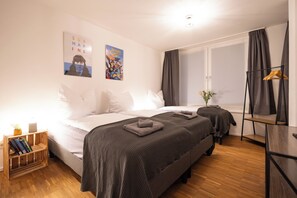 Ein Schlafzimmer mit Bett, Nachttischen, Holzboden, einem Fenster mit Vorhängen und Wandbildern.