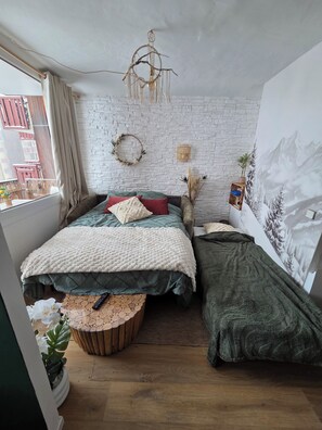 A bedroom with a bed, a side table, a wall-mounted light fixture, a window with curtains, and a mural on the wall. - Mountain apartment 5people ski in ski out la plagne bellecôte (La Plagne Tarentaise)