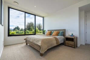 A bedroom with a large window, a bed, a bedside table, and a nightstand. - Stackbrae House with Mountain Views (Wānaka)