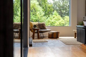Ein Zimmer mit großem Fenster, einer Couch, einem Sessel, einem kleinen Tisch und einem dekorativen Teppich.