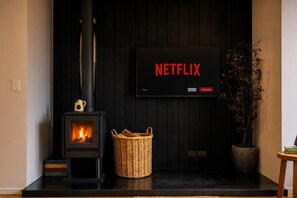 Ein modernes Wohnzimmer mit Kaminofen, flachbildfernseher an der Wand und einem Korbwäschesammler auf dem Boden.
