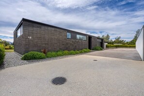 A modern building with a brick facade, a driveway, and a small garden area. - Stackbrae House with Mountain Views (Wānaka)
