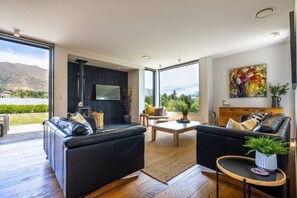 Ein modernes Wohnzimmer mit Kamin, großen Fenstern und Blick ins Freie.