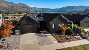 A modern building with a garage, surrounded by a landscaped area with trees, set against a mountainous backdrop.
