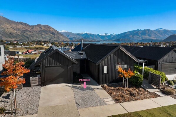 A modern building with a garage, surrounded by a landscaped area with trees, set against a mountainous backdrop.
