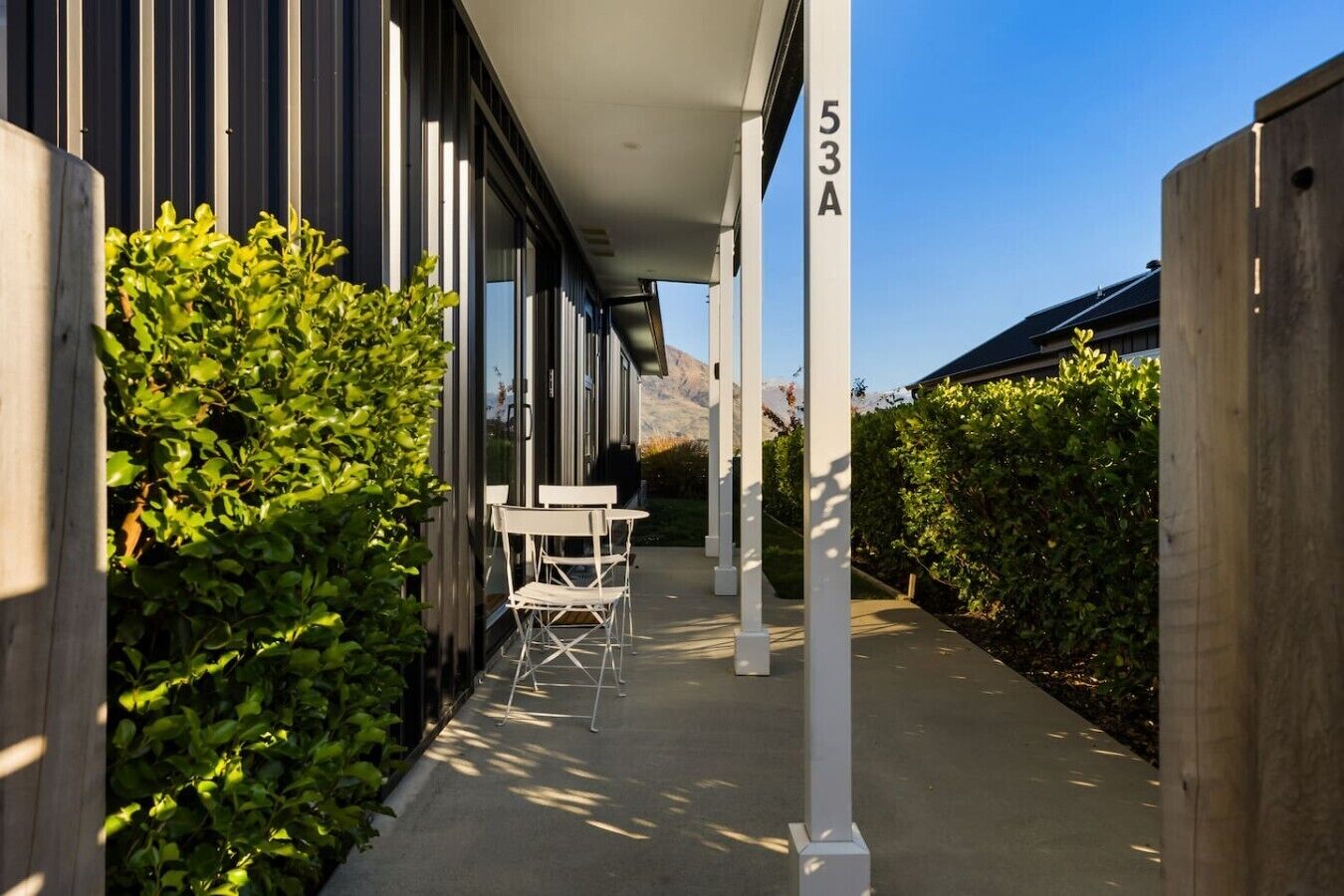 A covered outdoor area with a row of white chairs, a wooden fence, and a building with a number '53A' on it.