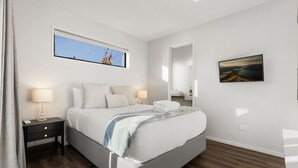 A modern bedroom with a bed, bedside tables, a window, a mirror, and a painting on the wall.