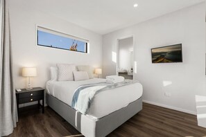 Ein modernes Schlafzimmer mit Bett, Nachttischen, einem Fenster, einem Spiegel und einem Bild an der Wand.