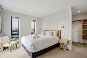 A modern bedroom with a large bed, a chair, a bedside table, and a wardrobe. - Architectural Northlake Retreat | Sleeps 8, Wood-Burning Fireplace, Media Room & Covered Outdoor Deck (Wānaka)