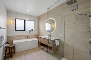 A modern bathroom with a bathtub, a glass-enclosed shower, a vanity with a mirror, and a window. - Architectural Northlake Retreat | Sleeps 8, Wood-Burning Fireplace, Media Room & Covered Outdoor Deck (Wānaka)