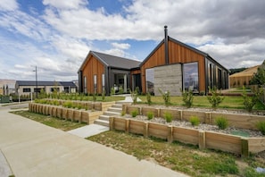Ein modernes Gebäude mit Holzfassade, großen Fenstern und einem angelegten Garten mit Stufen zum Eingang.