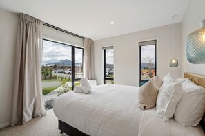 Ein Hotelzimmer mit einem großen Bett, zwei Fenstern, Blick ins Freie und einer Hängelampe.