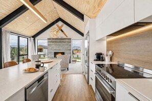 Eine moderne Küche mit Kamin, Holzbalkendecke und Blick ins Freie.