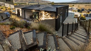 Um edifício moderno com telhado plano, rodeado por um jardim com diversas plantas e um deck de madeira.