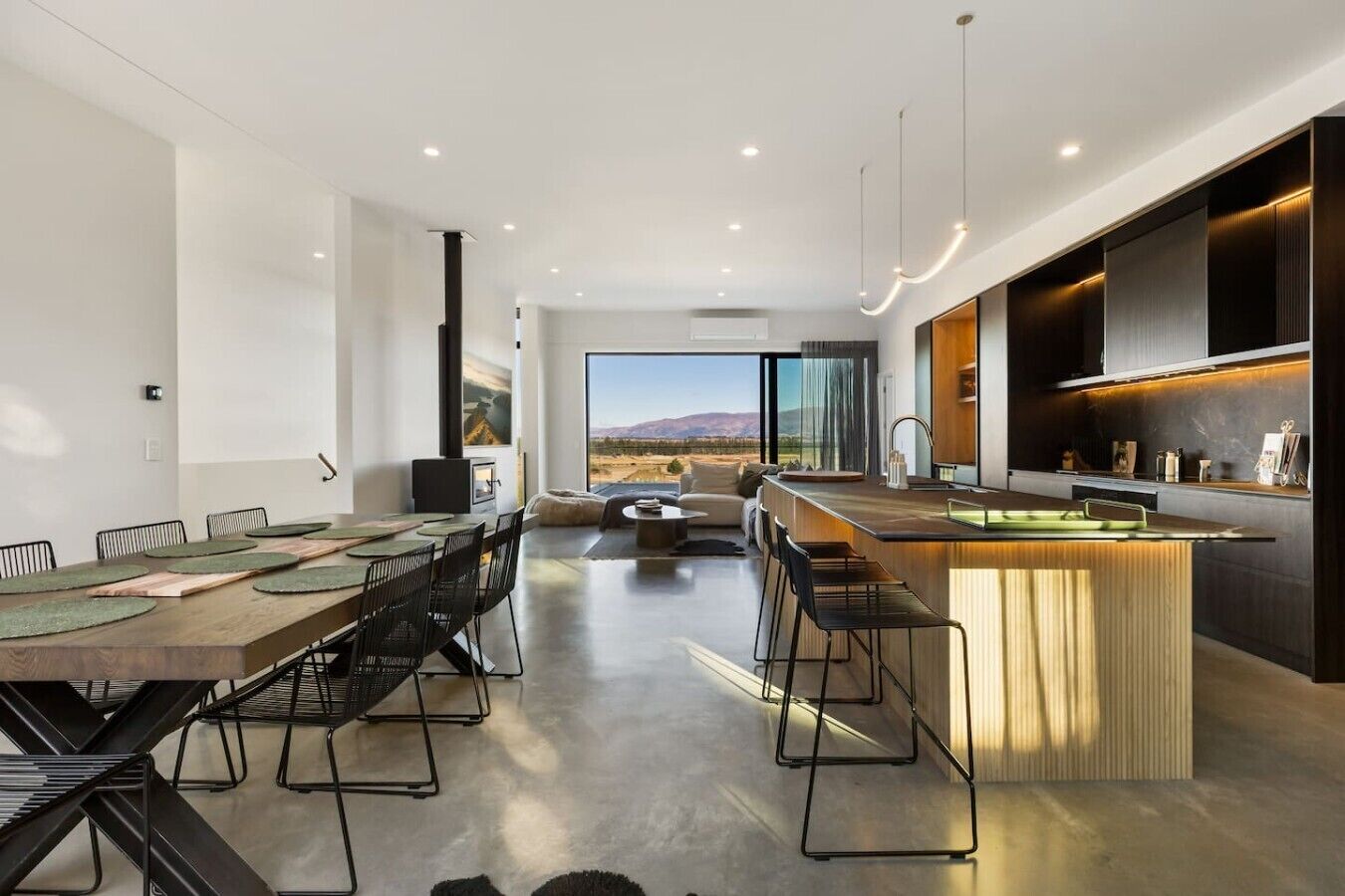 A modern kitchen with a central island, dining area with chairs, and a view of the outdoors.