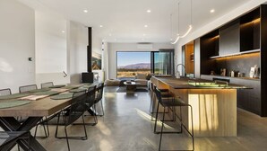 Cozinha moderna com ilha central, área de jantar com cadeiras e vista para o exterior.