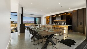 Cozinha moderna com uma ilha central, área de jantar com uma mesa grande e cadeiras, e vista para uma paisagem montanhosa através de janelas amplas.