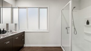 Un bagno moderno con cabina doccia in vetro, un'ampia finestra e pavimento in legno scuro.