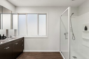 Ein modernes Badezimmer mit Duschkabine aus Glas, einem großen Fenster und Holzboden in Dunkelholzoptik.